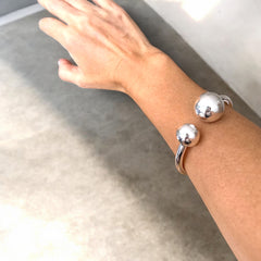 pulseraBangle de acero plateado con diseño abierto y esferas en los extremos. Minimalista y elegante.