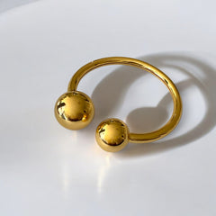 Bangle de acero dorado con diseño abierto y esferas en los extremos. Minimalista y elegante.