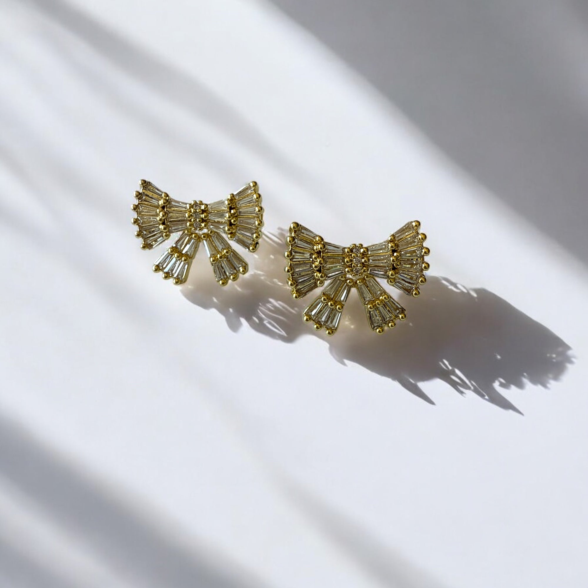 Aretes lazo dorado con circones blancos en acero bañado en oro, diseño femenino y sofisticado.