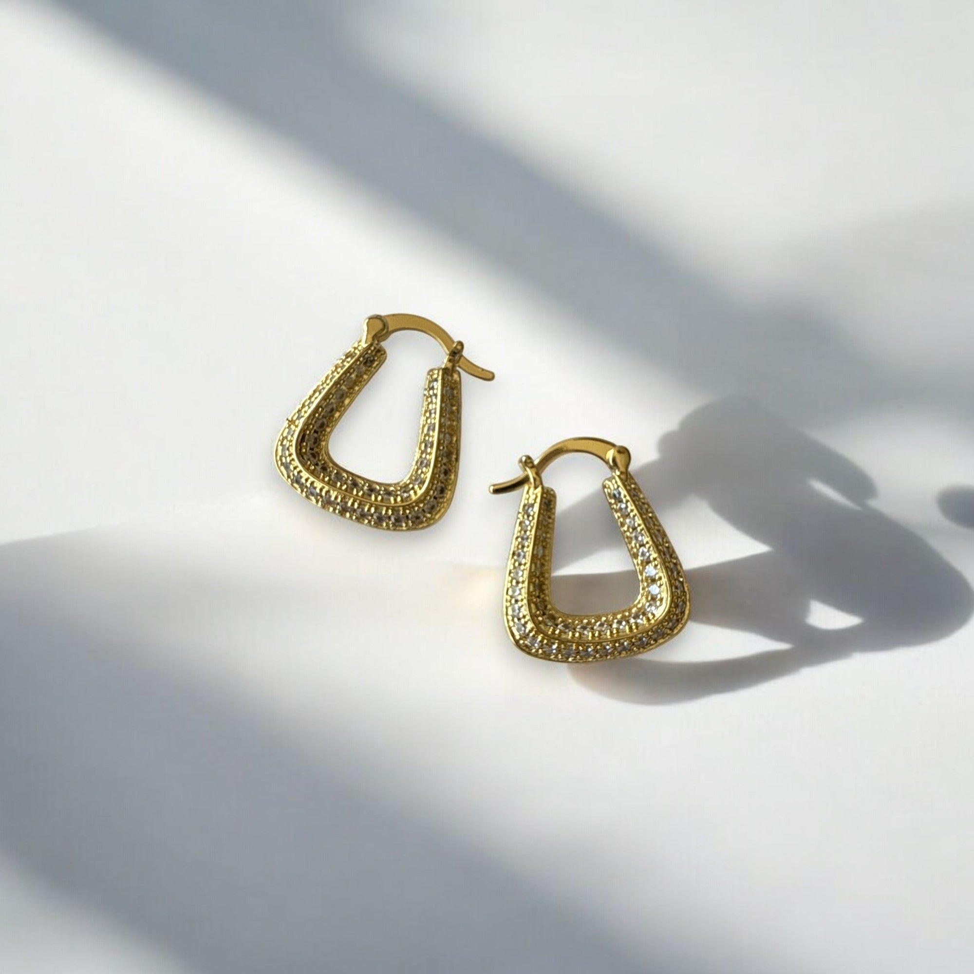 Aretes dorados con circones en diseño geométrico sobre fondo blanco.