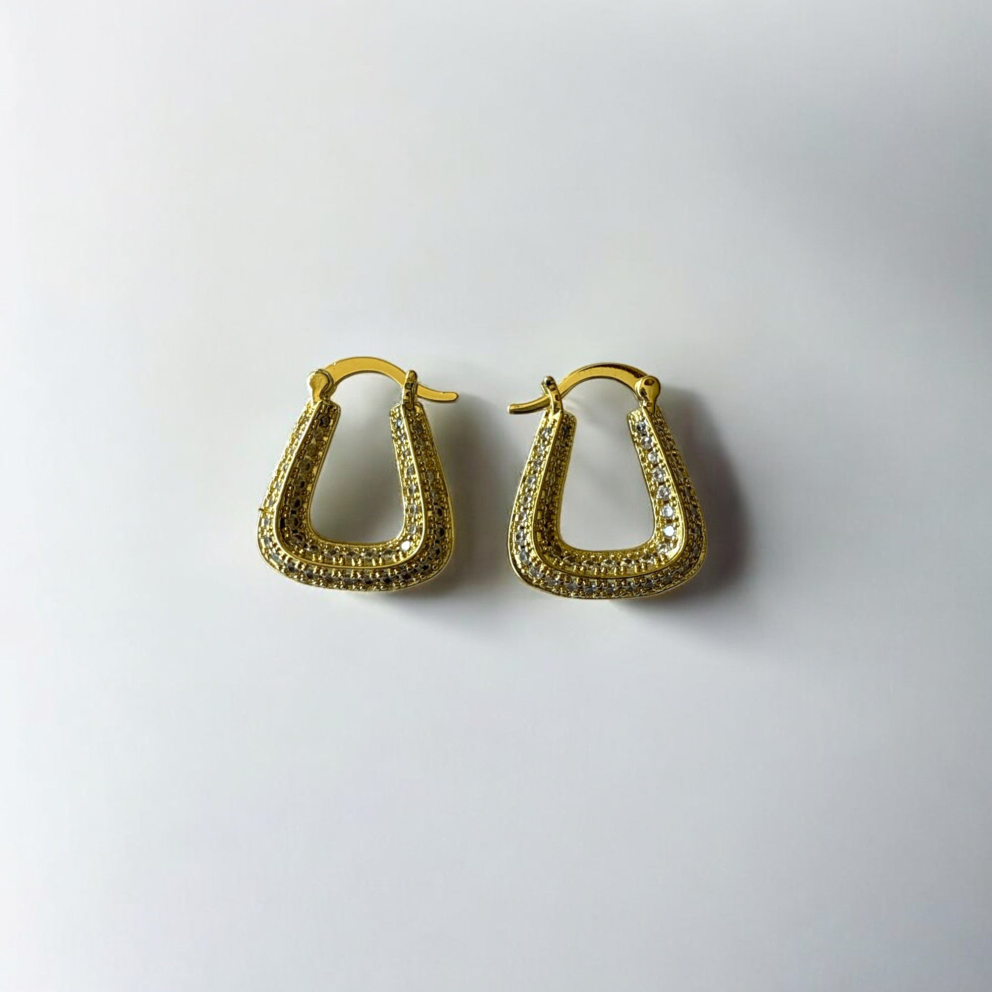 Aretes dorados con circones en diseño geométrico sobre fondo blanco.