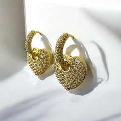 Aretes dorados con dije de corazón y circones sobre fondo blanco.