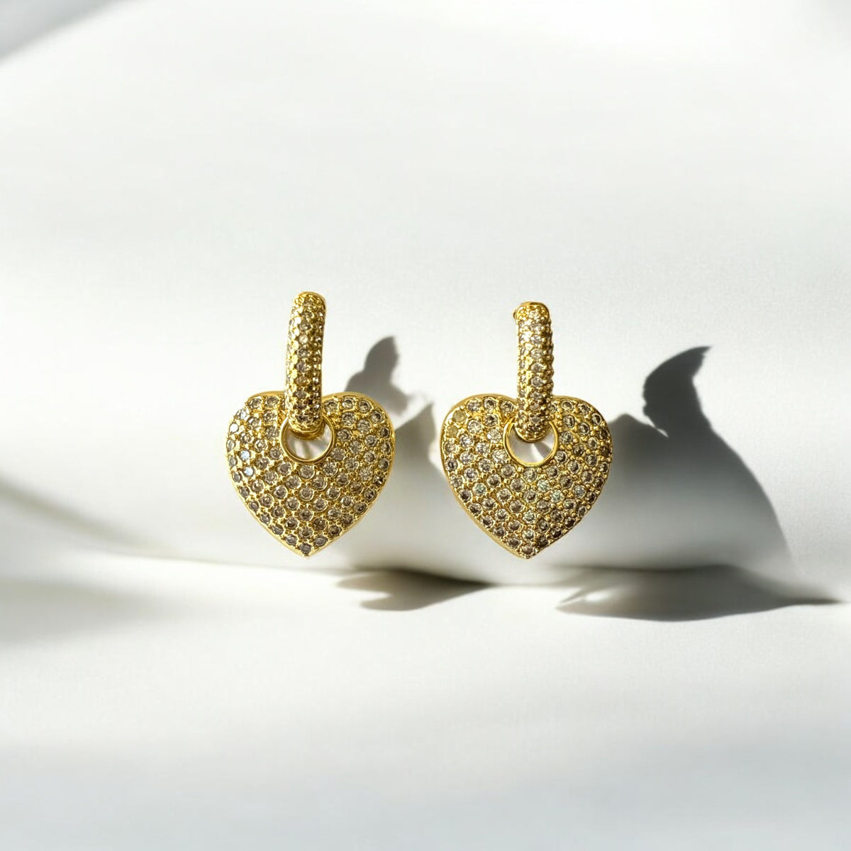 Aretes dorados con dije de corazón y circones sobre fondo blanco.