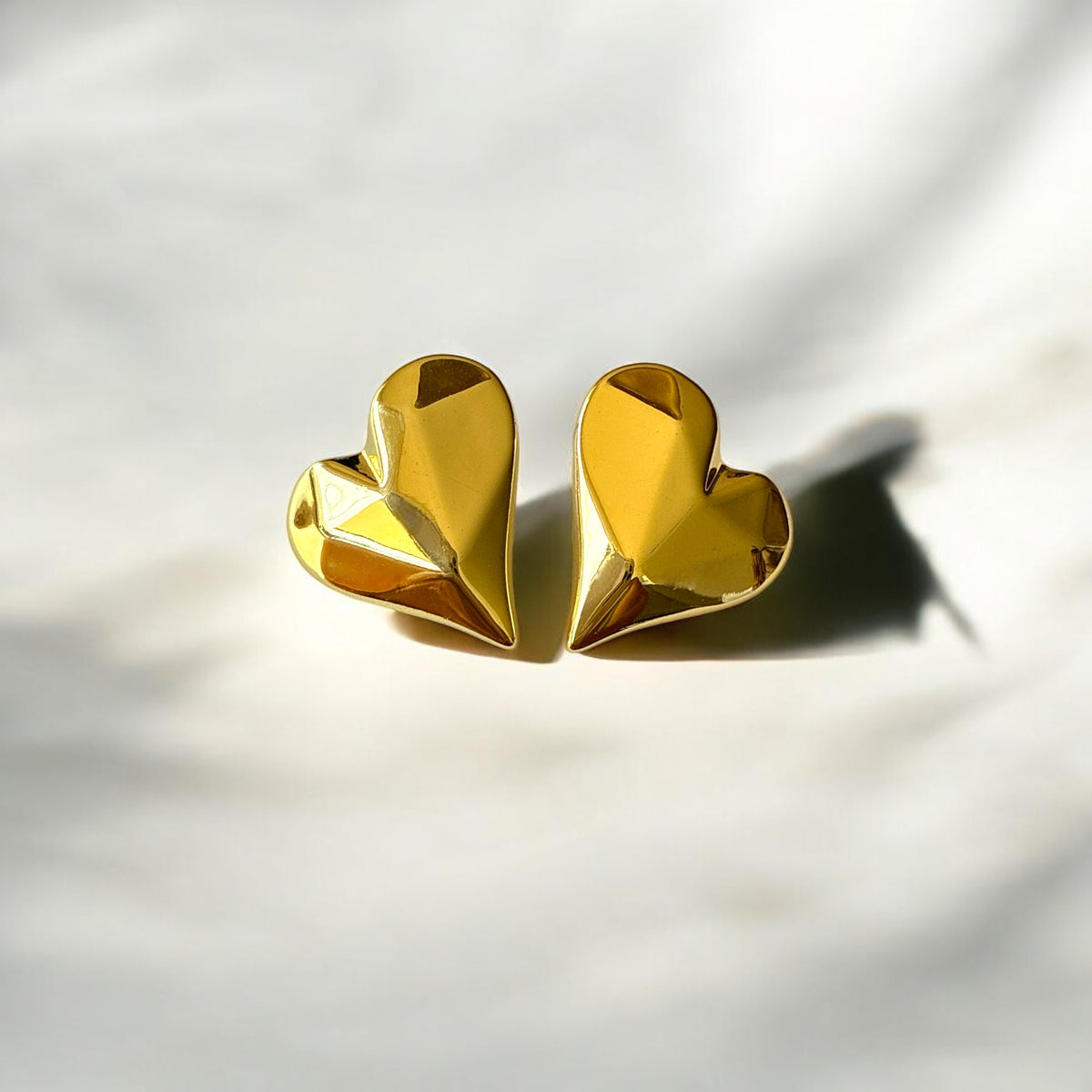 Aretes corazón facetado de acero dorado en alto relieve.