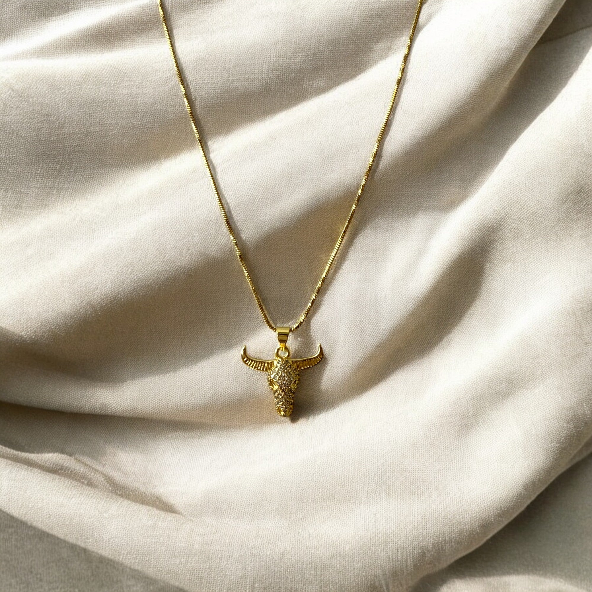 Collar de acero bañado en oro con dije de toro y circones transparentes. Cadena fina de 1 mm, regulable. Diseño imponente y elegante.