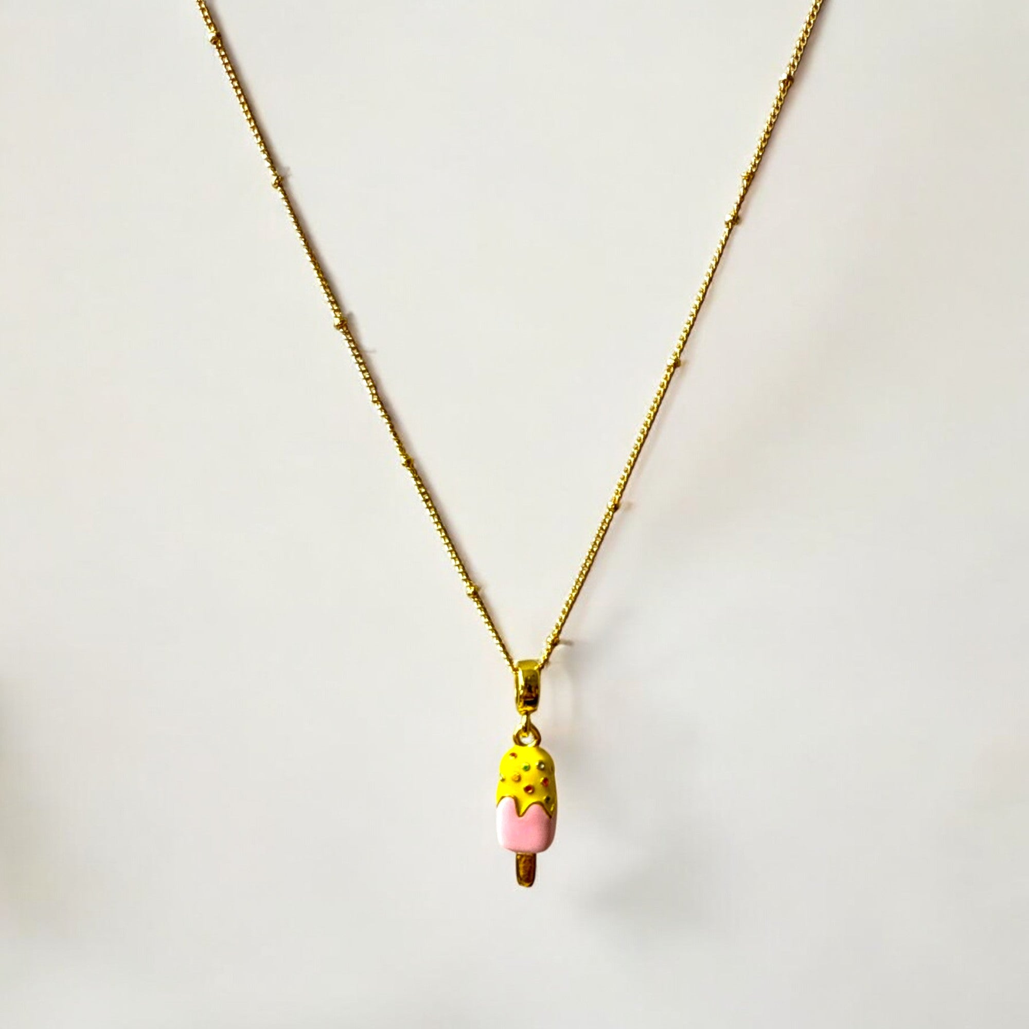 Collar de acero bañado en oro con dije de helado esmaltado en colores vibrantes y cadena satélite de 1 mm y 45 cm, regulable. Diseño delicado y juvenil.